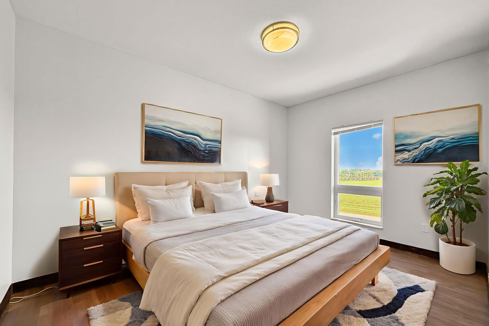 Aerial view of a multi-story apartment building with balconies, light-colored brick, and a large parking lot. Blue sky in the background.