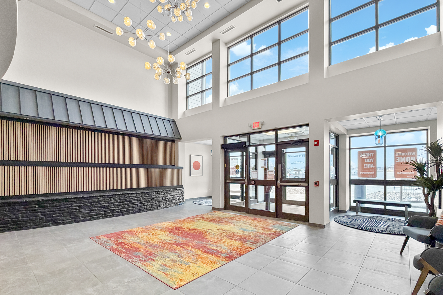 Apartment building with stone accents, balconies, and parked cars on a grassy lawn under a blue sky.