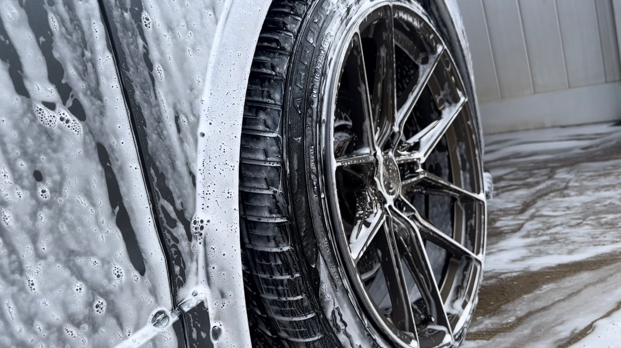 A person wearing orange gloves is polishing a black car with a cloth.