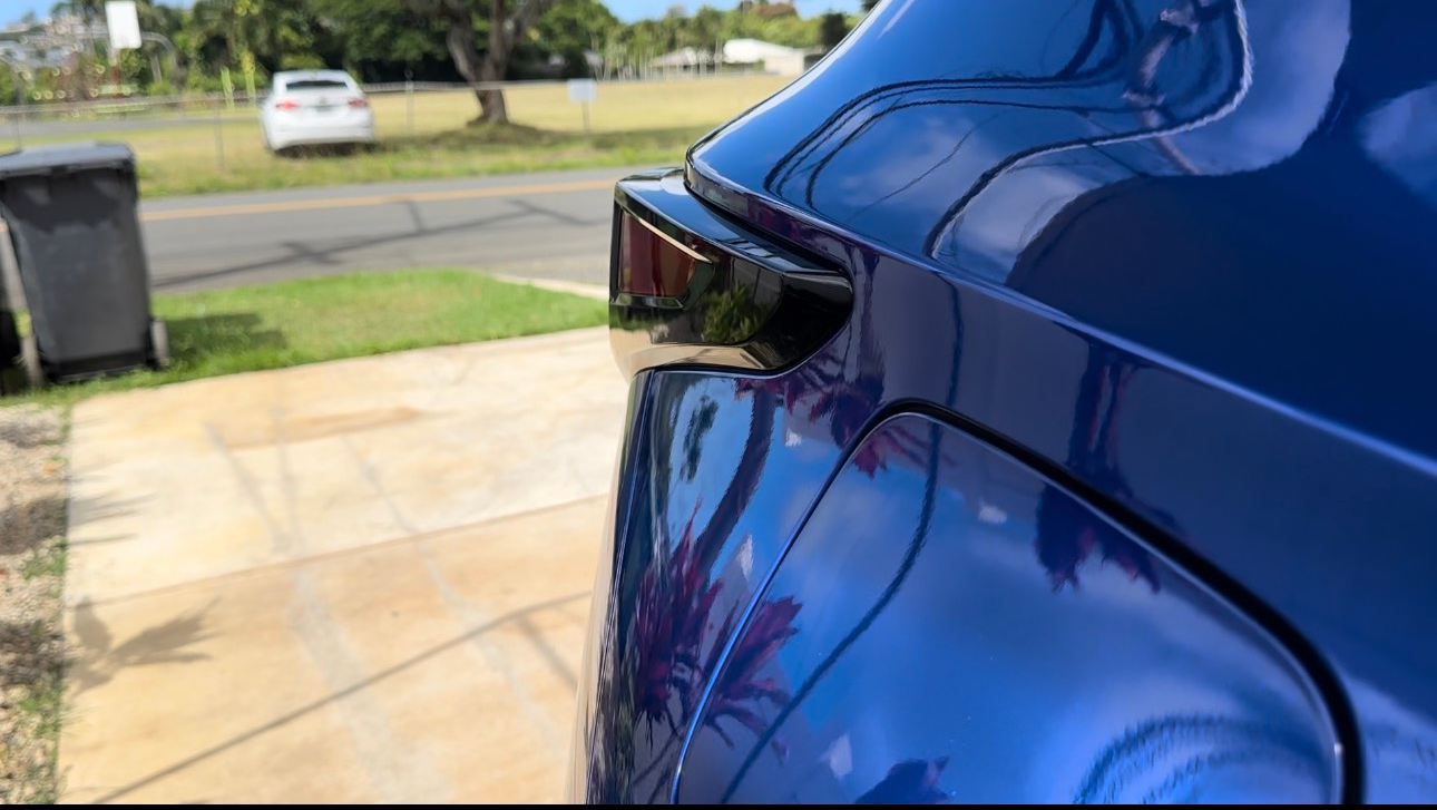 A blue car is parked in a driveway next to a road.