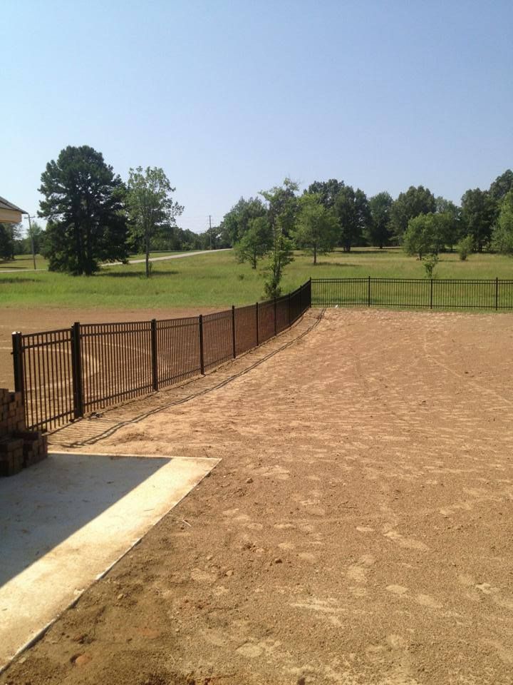A fence surrounds a dirt field with trees in the background