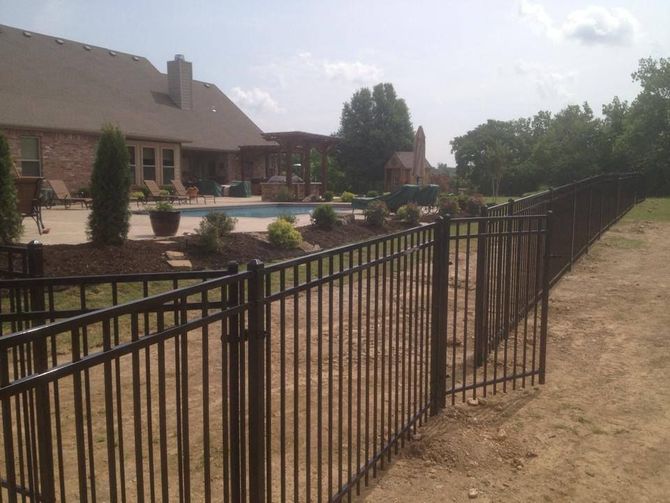 A metal fence surrounds a backyard with a pool and a house in the background.