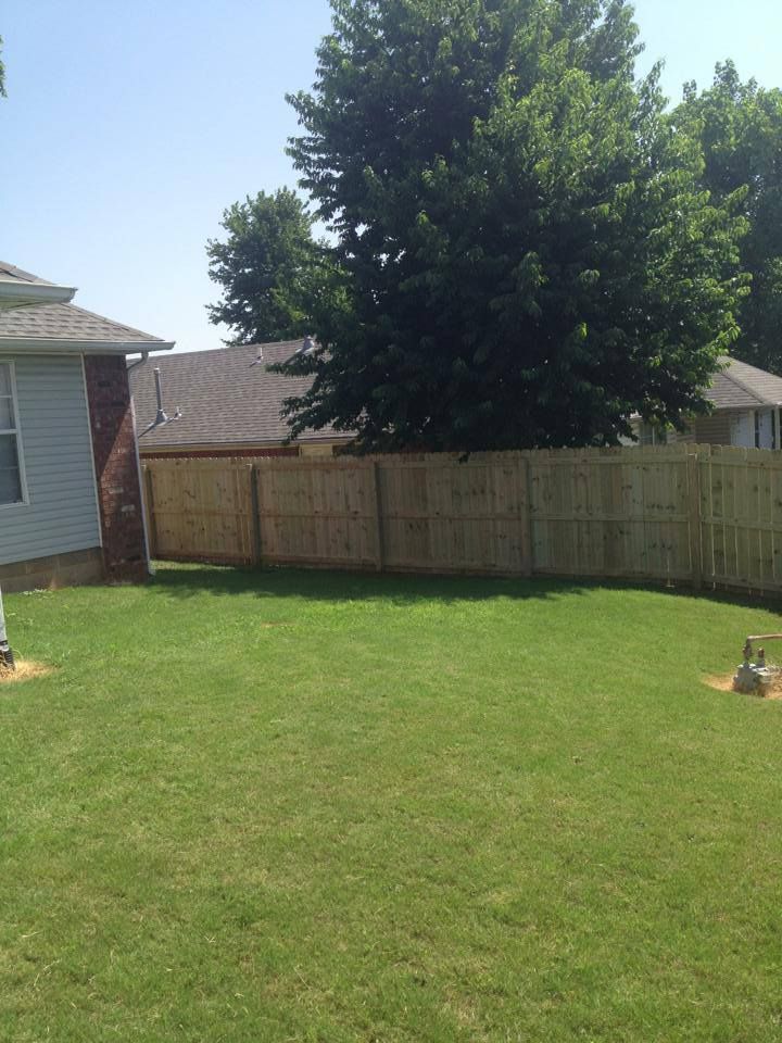A backyard with a wooden fence and a house in the background