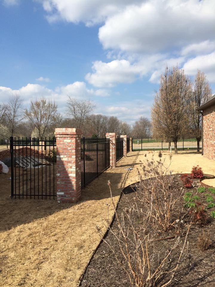 A brick walkway leading to a house with a fence and a brick pillar.