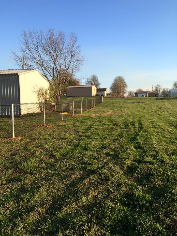 A large grassy field with a fence and a shed in the background.