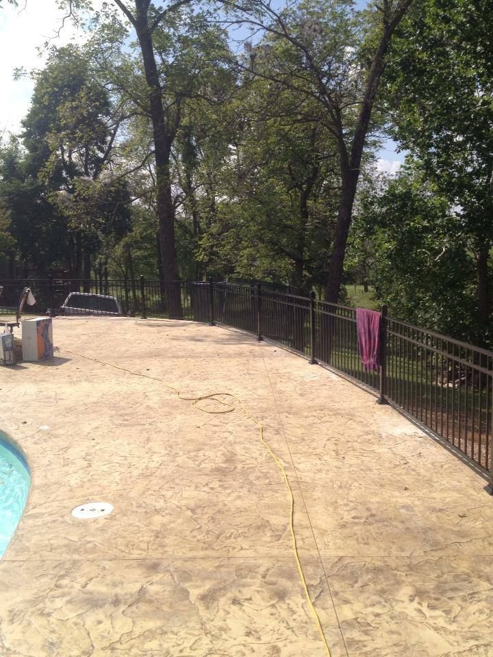 A fence surrounds a swimming pool with trees in the background.