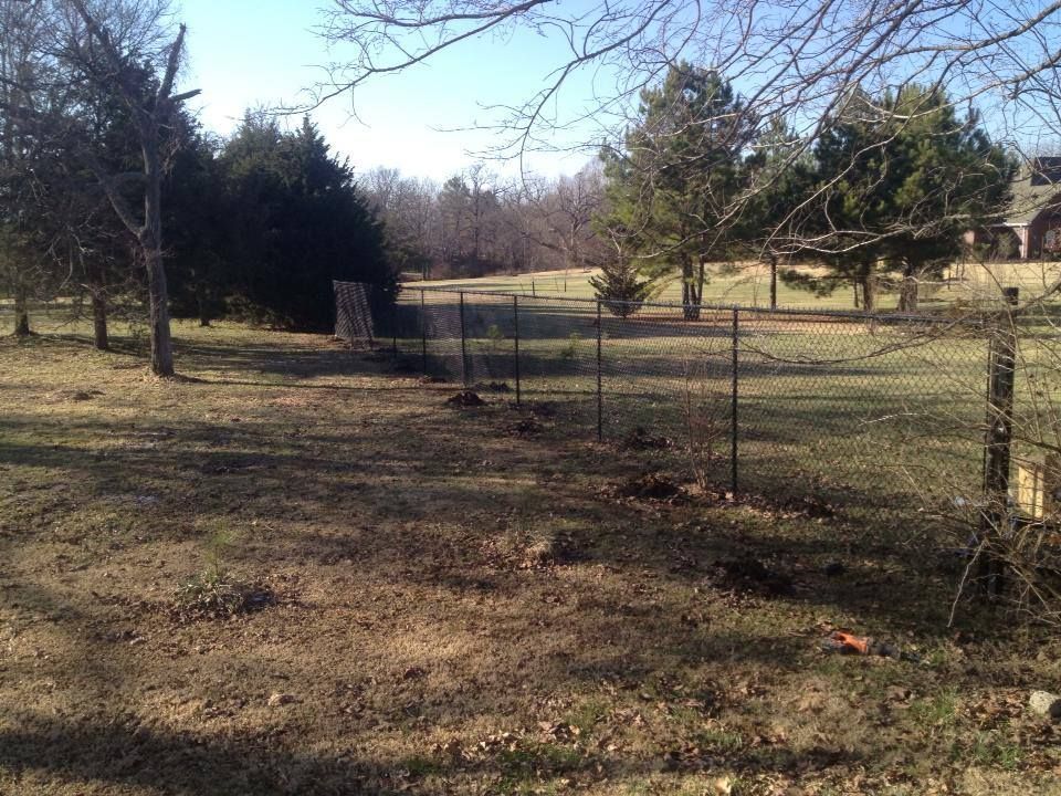 There is a fence in the middle of a field with trees in the background.