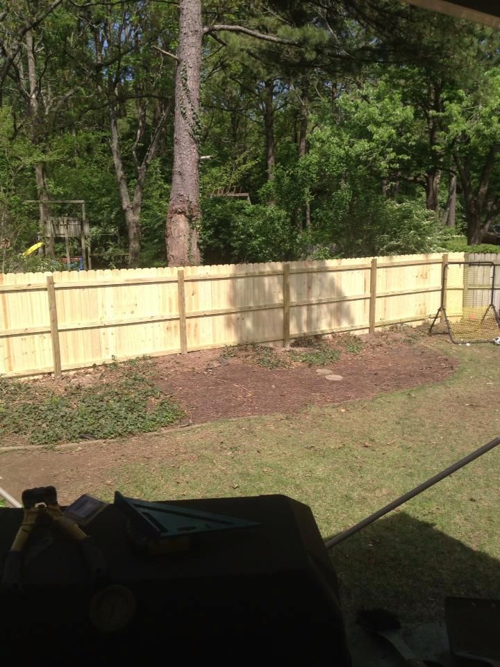 A wooden fence in a backyard with trees in the background.