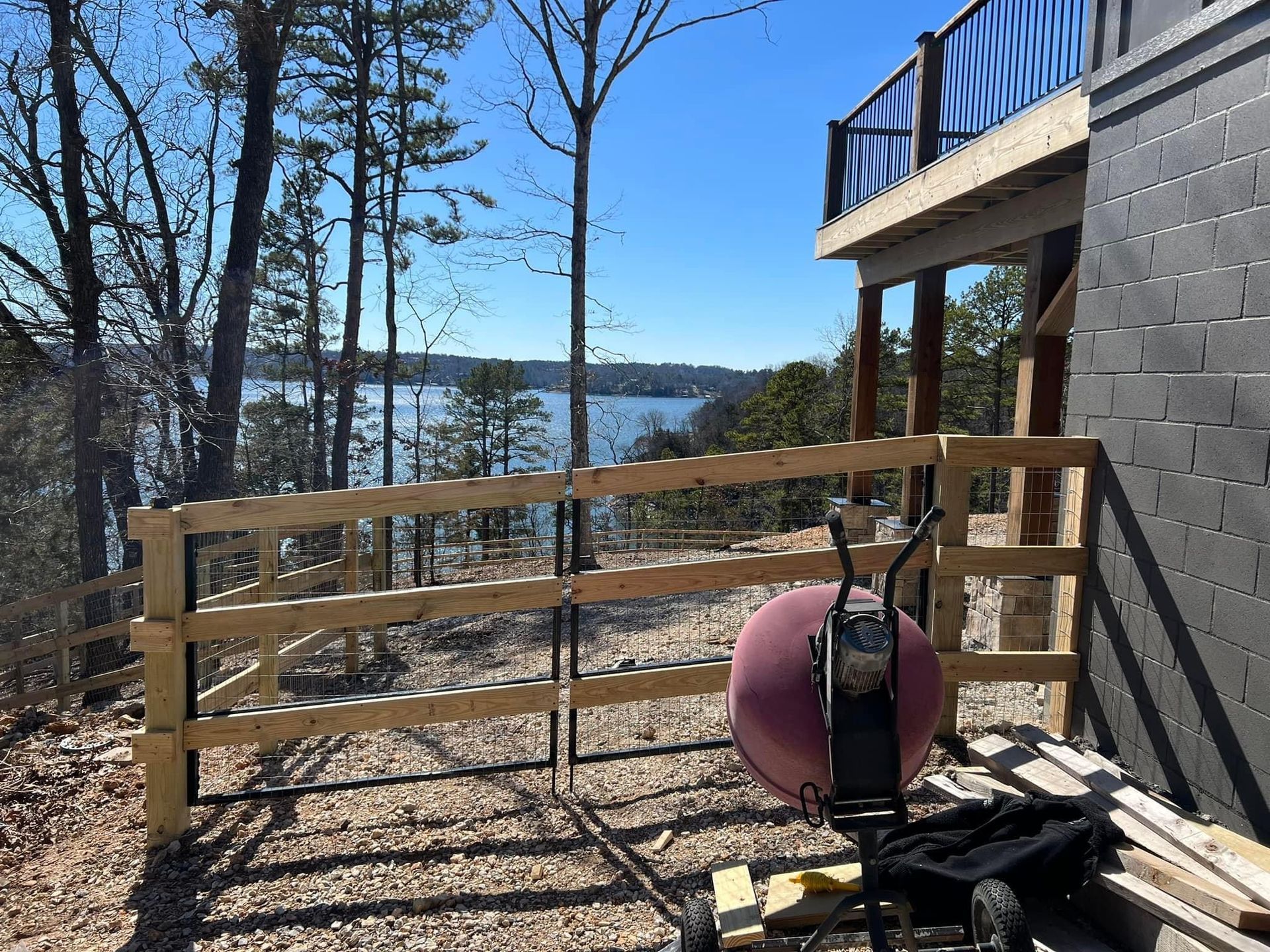 A wooden fence is being built in front of a house with a view of a lake.