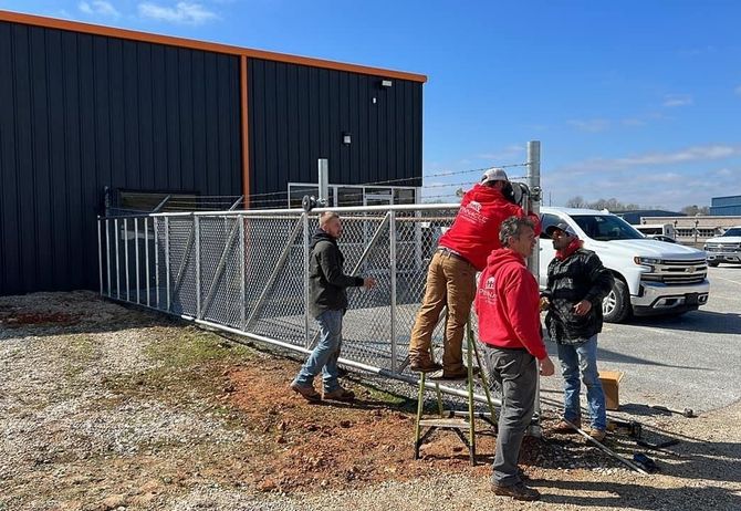 A group of men are working on a chain link fence in front of a building.