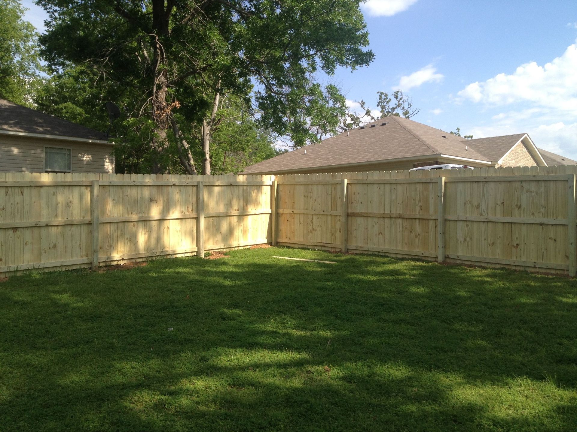 A wooden fence surrounds a lush green yard in front of a house.