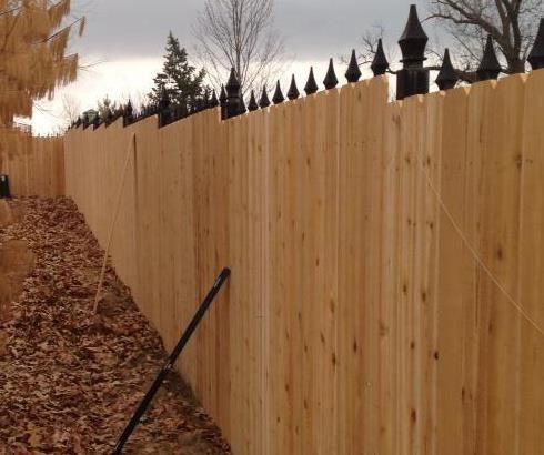 A wooden fence with black spikes is surrounded by leaves and a rake.