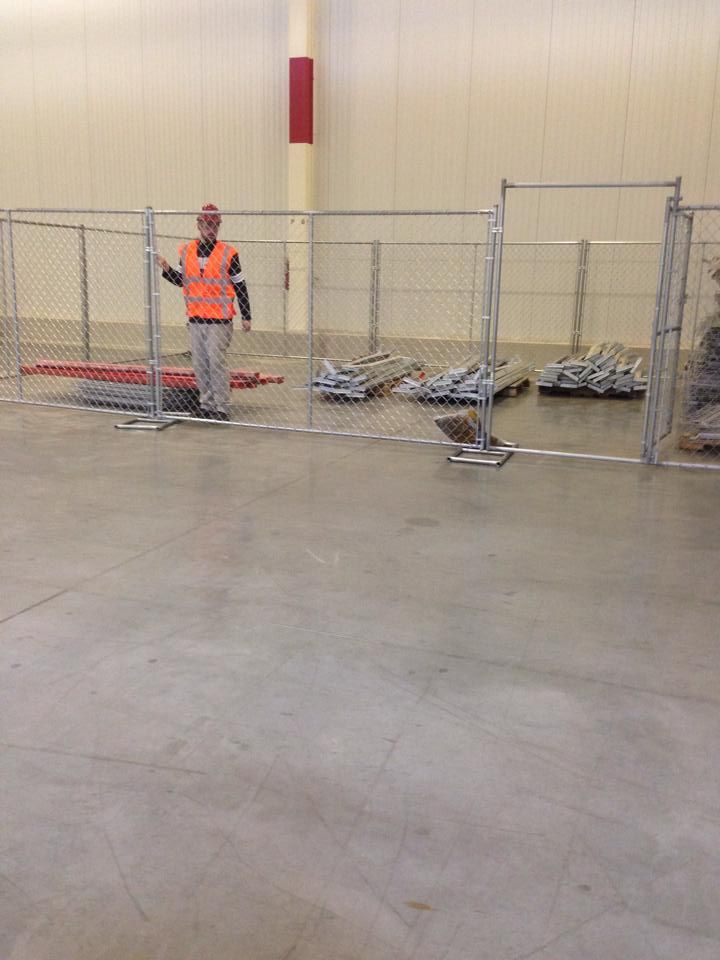 A man in an orange vest is standing in front of a fence.