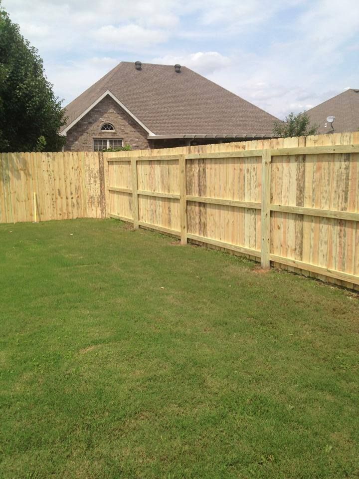 A wooden fence surrounds a lush green lawn in front of a house.