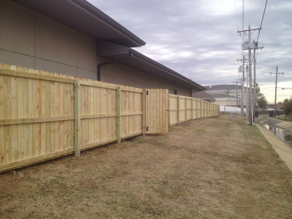 A wooden fence surrounds a grassy area in front of a building.
