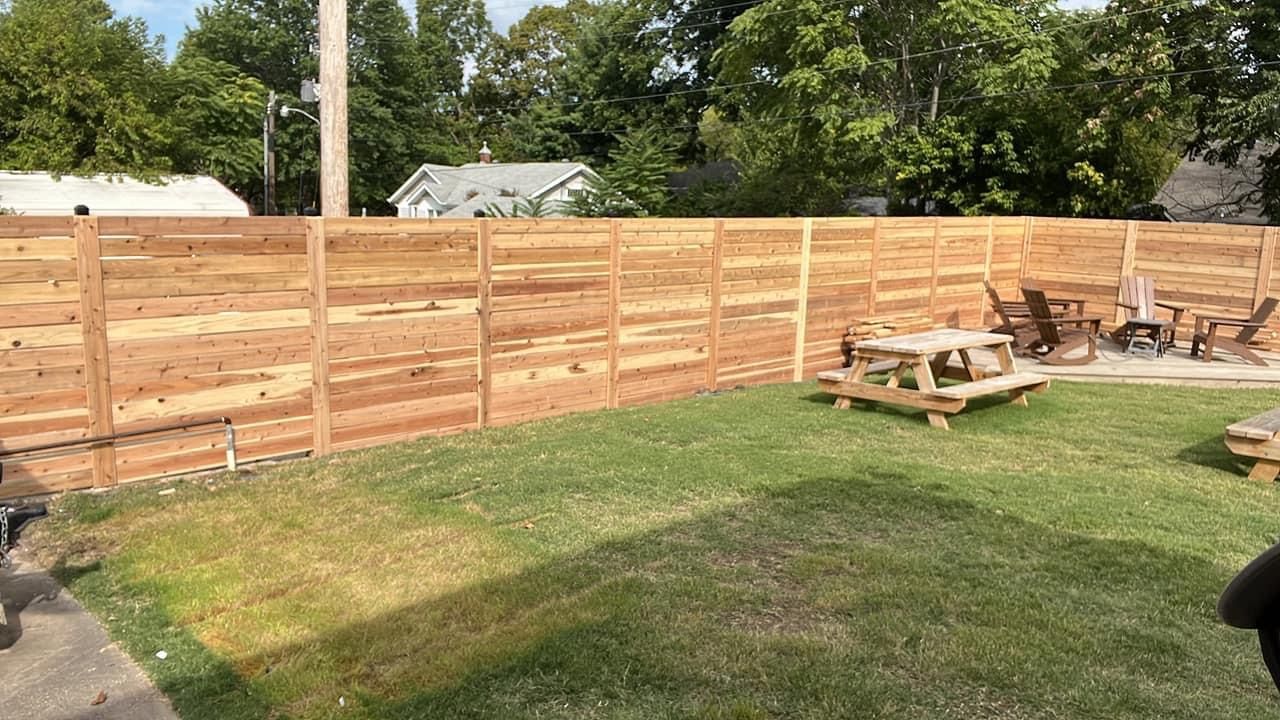 A wooden fence surrounds a backyard with a picnic table and chairs.