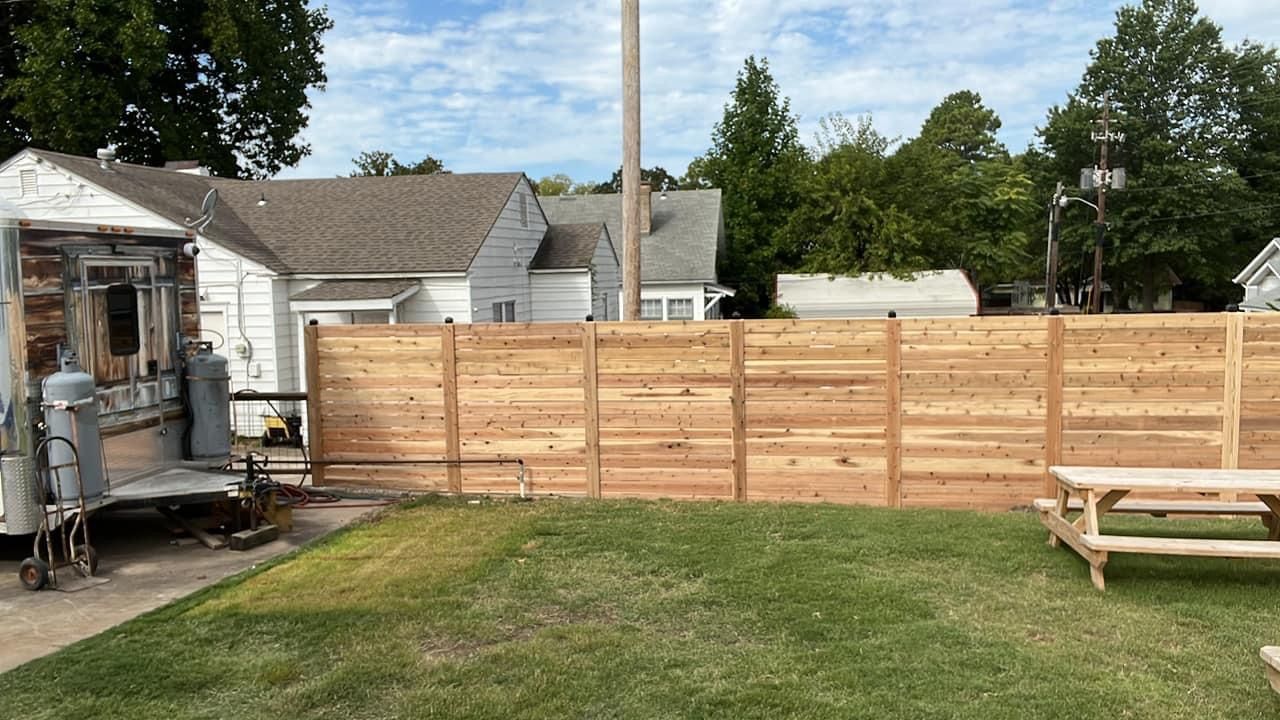 A wooden fence surrounds a lush green yard with a picnic table.