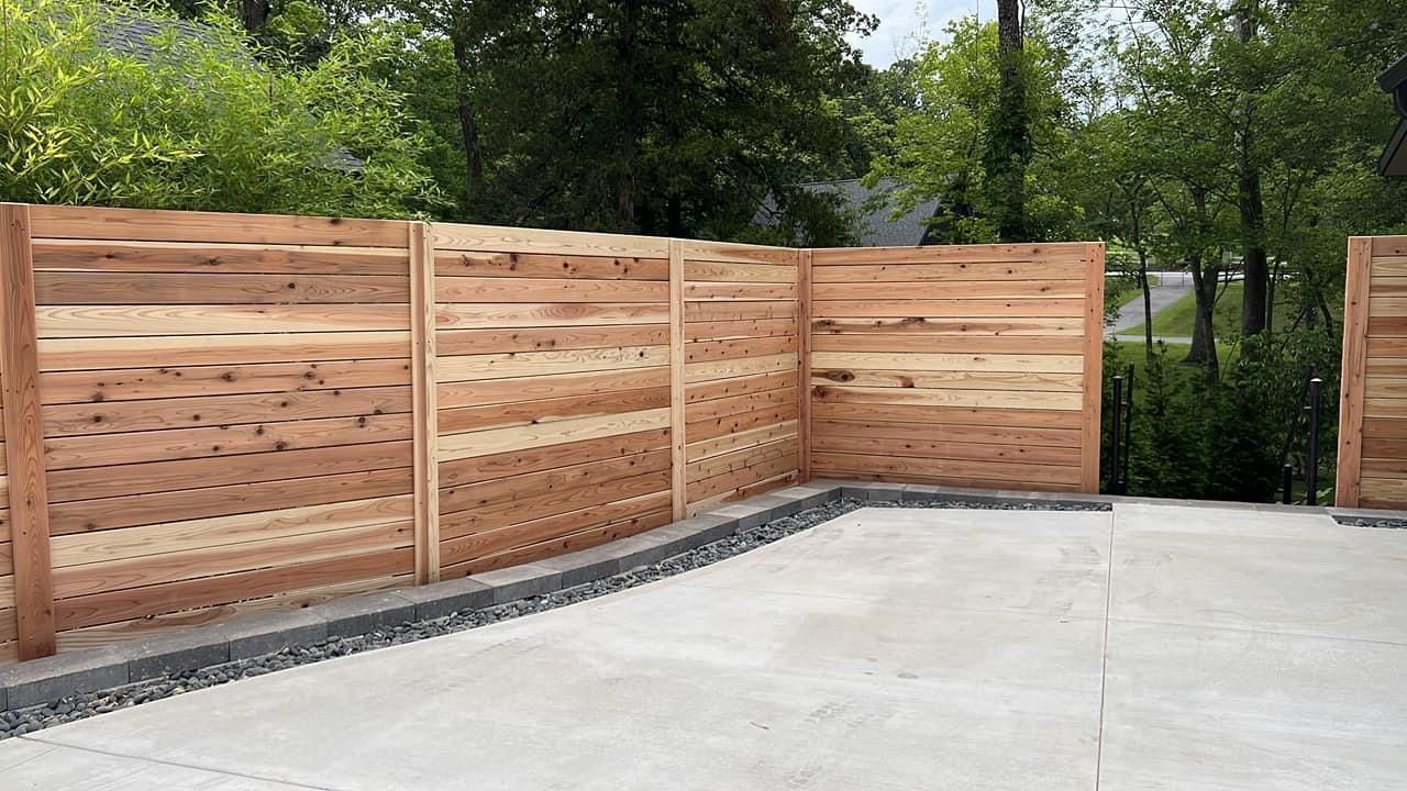 A wooden fence is surrounding a concrete driveway.