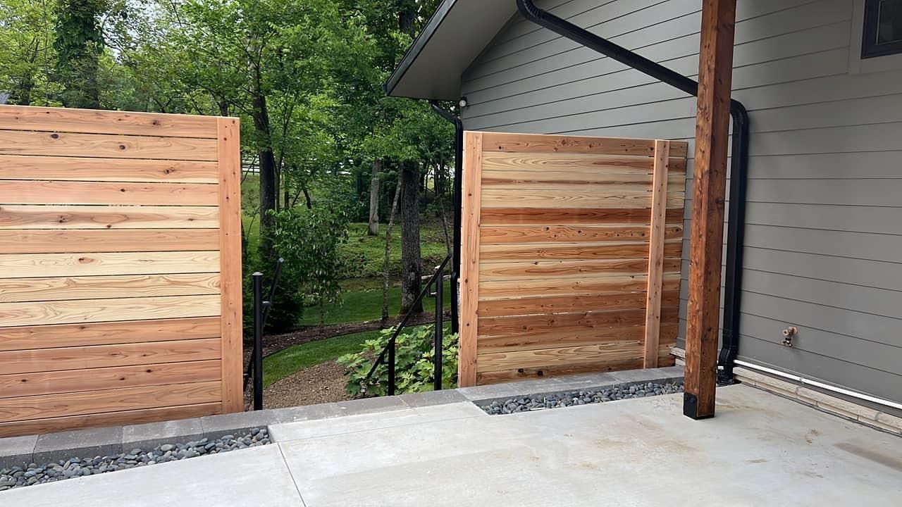 A wooden fence is surrounding a concrete patio next to a house.