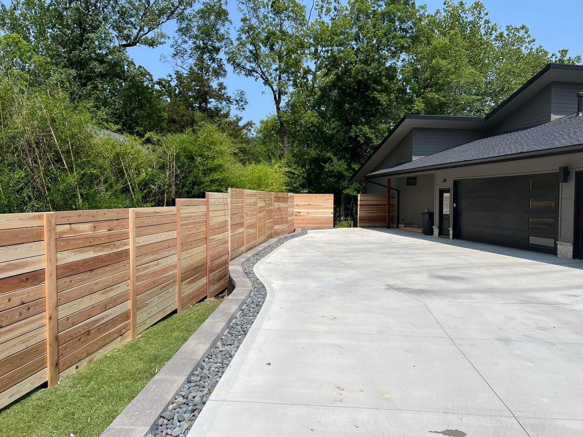 A wooden fence surrounds a driveway leading to a house.