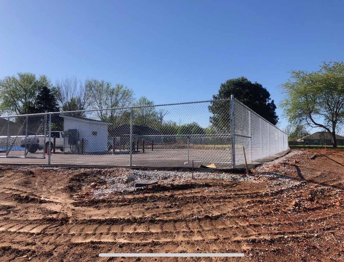 A metal fence is surrounding a dirt field.