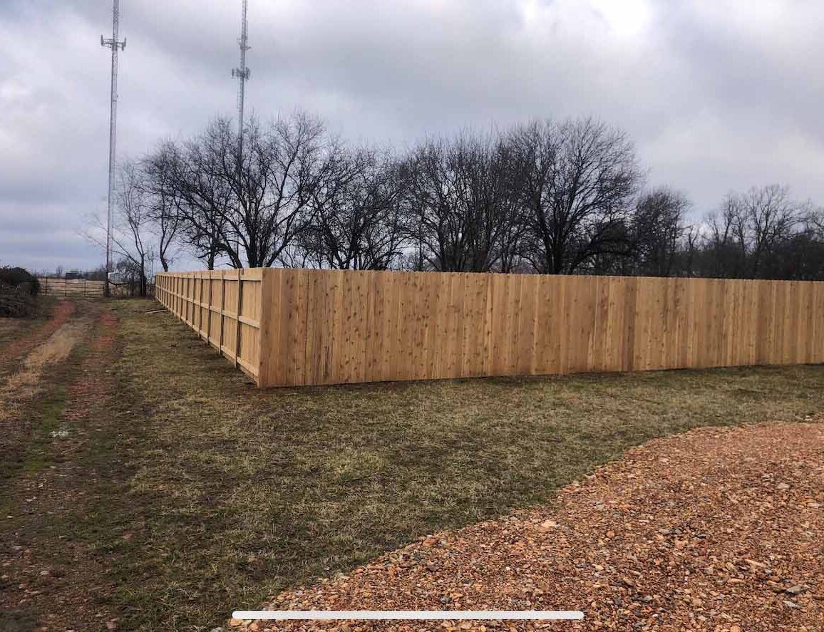 A wooden fence surrounds a grassy field with trees in the background.