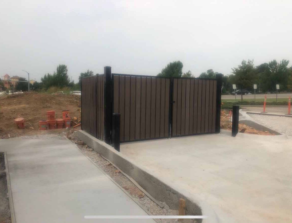 A wooden fence is sitting next to a concrete walkway in a parking lot.
