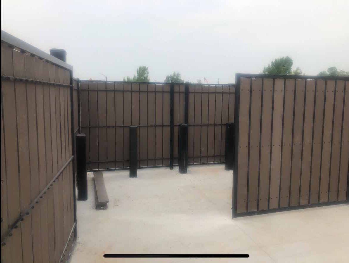 A fence made of wood and metal is surrounding a concrete area.