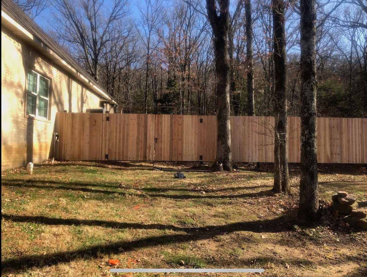 A wooden fence is in the backyard of a house surrounded by trees.