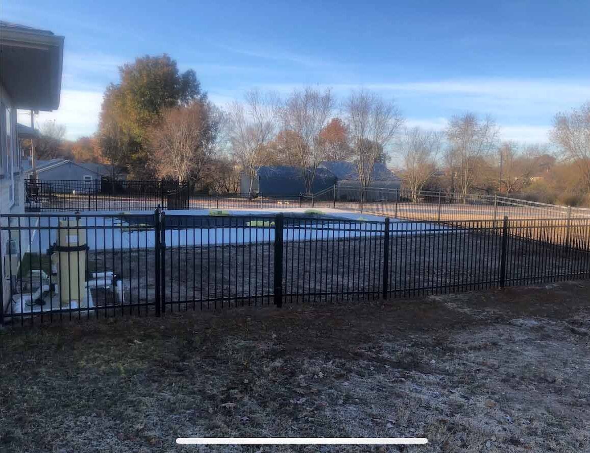 A metal fence surrounds a yard with a swimming pool in the background.