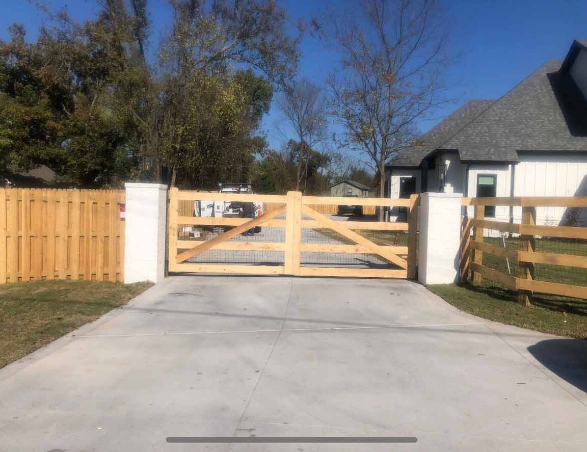 A wooden gate is sitting on the side of a driveway next to a house.
