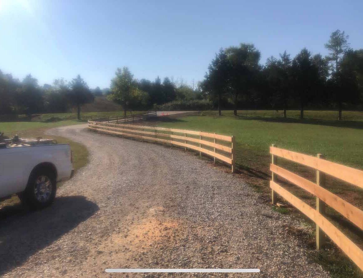 A white truck is parked on the side of a gravel road next to a wooden fence.