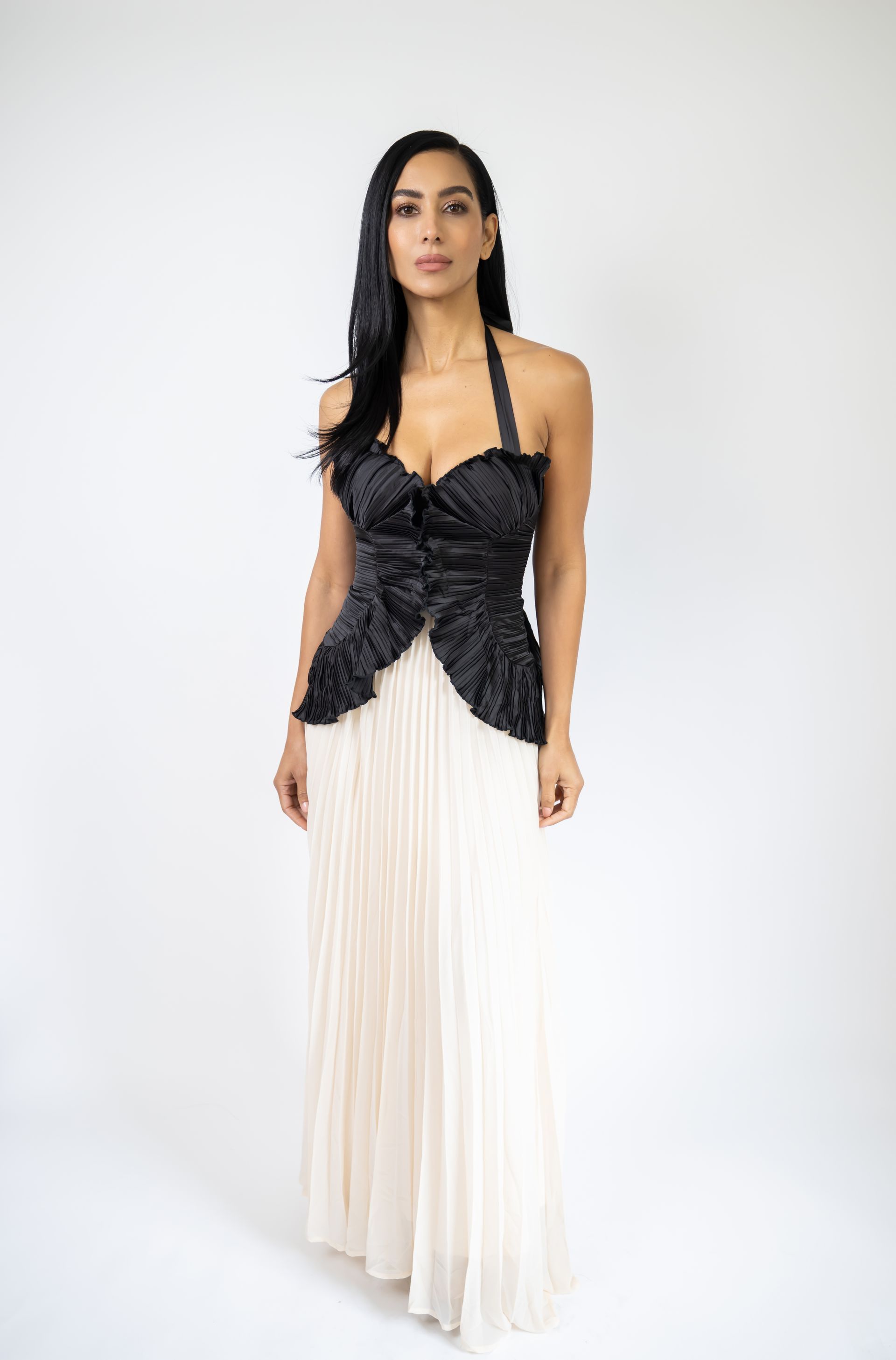 Woman in a white dress with black trim, standing against a mottled gray backdrop, holding up her skirt.