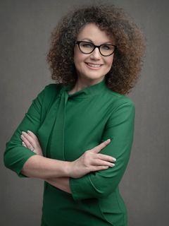 A woman wearing glasses and a green shirt is standing with her arms crossed.