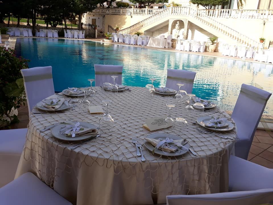 tavolo imbandito per un matrimonio con piatti e bicchieri davanti a una piscina