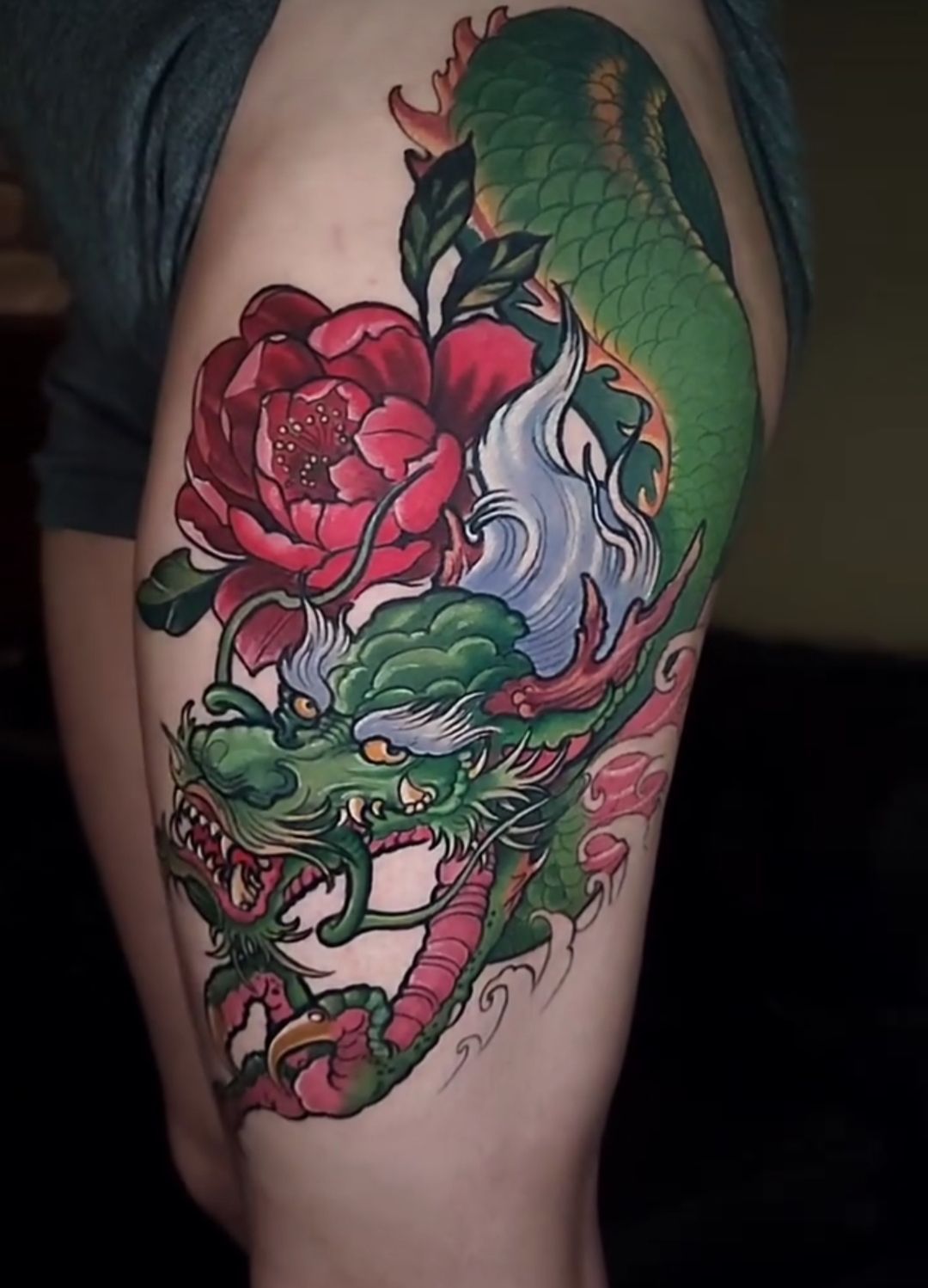 Green dragon and red flower tattoo on a person's thigh.
