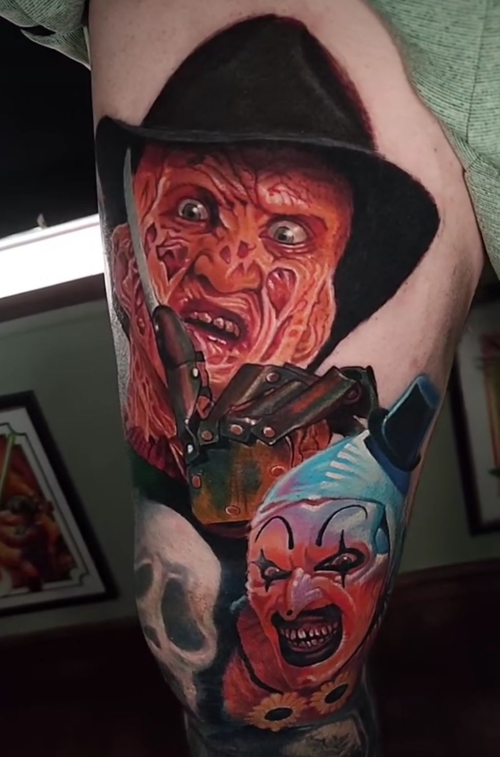 Tattoo of Freddy Krueger and a clown, in color, on a leg. Krueger with glove, scary face. Clown smiling.