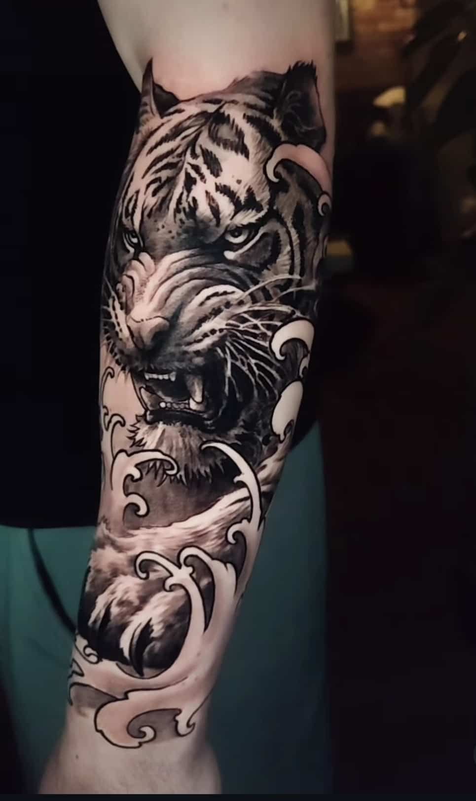 Black and white tiger tattoo on an arm, showing a snarling tiger head with ocean waves.