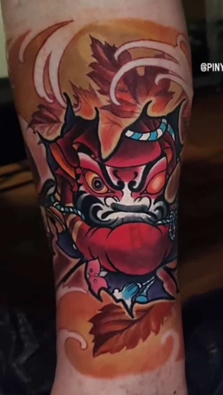 Japanese style oni tattoo on calf, red and orange colors, surrounded by autumn leaves and water waves.