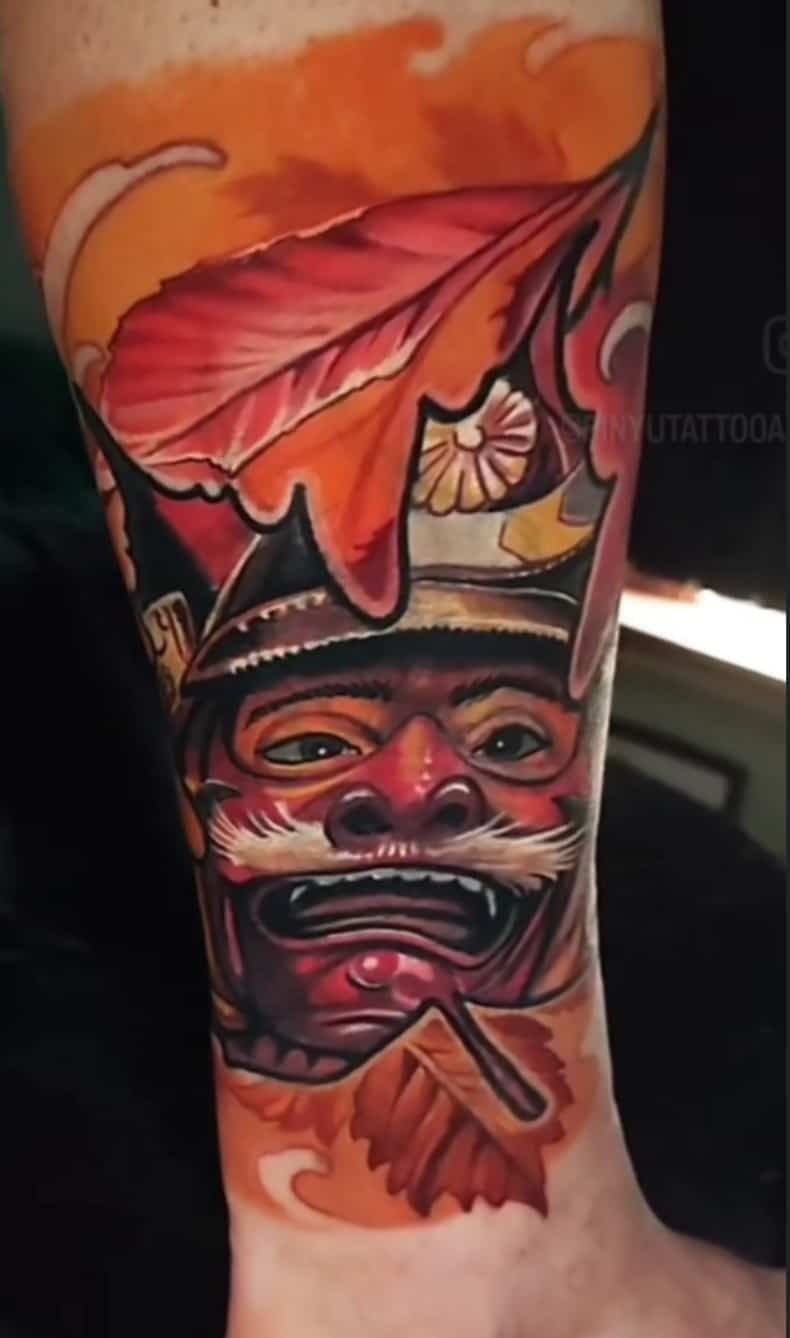Tattoo of a red Oni mask, with a leaf, and orange and yellow background.