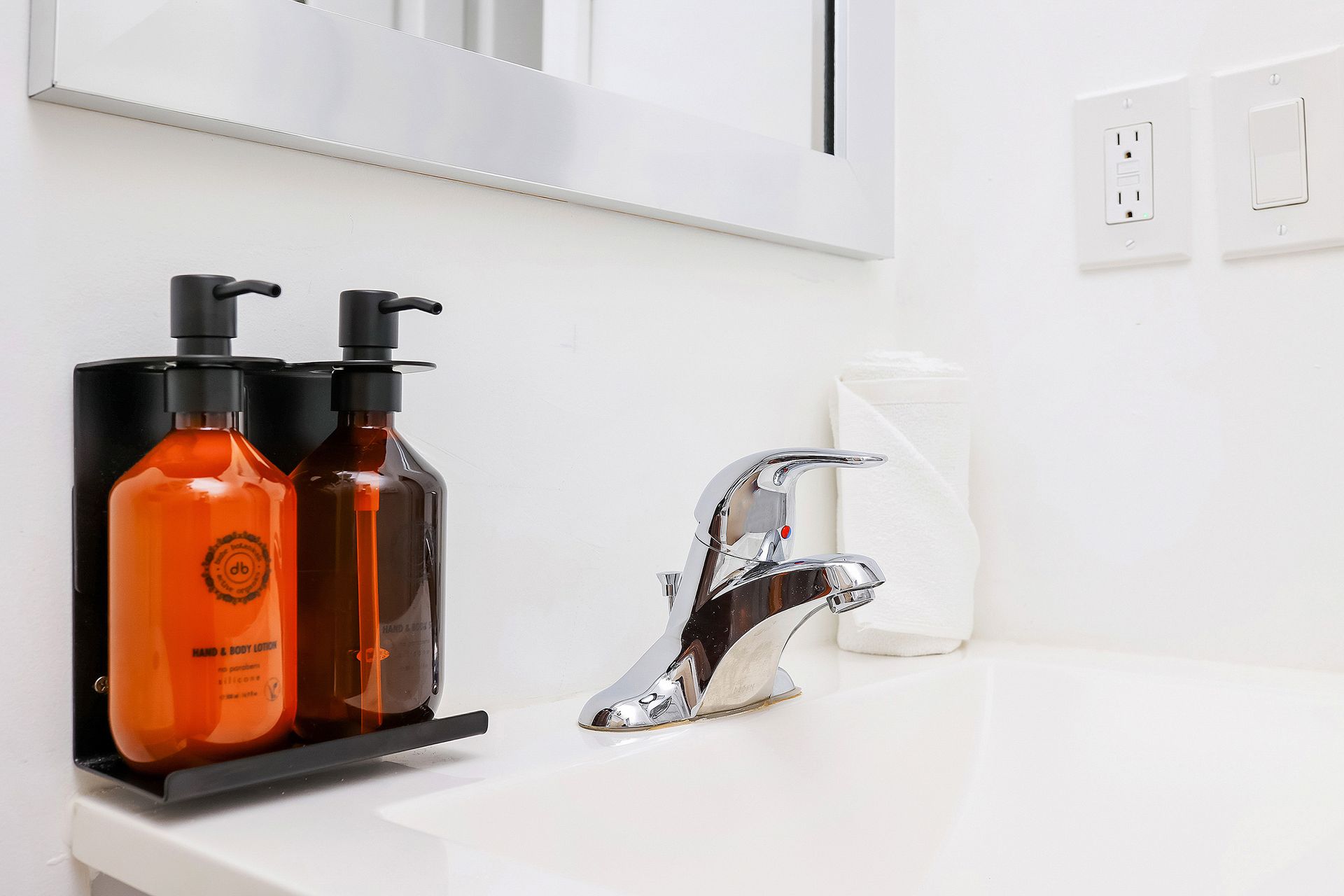 Bathroom sink with soap dispensers and faucet. White countertop, mirror, and wall.