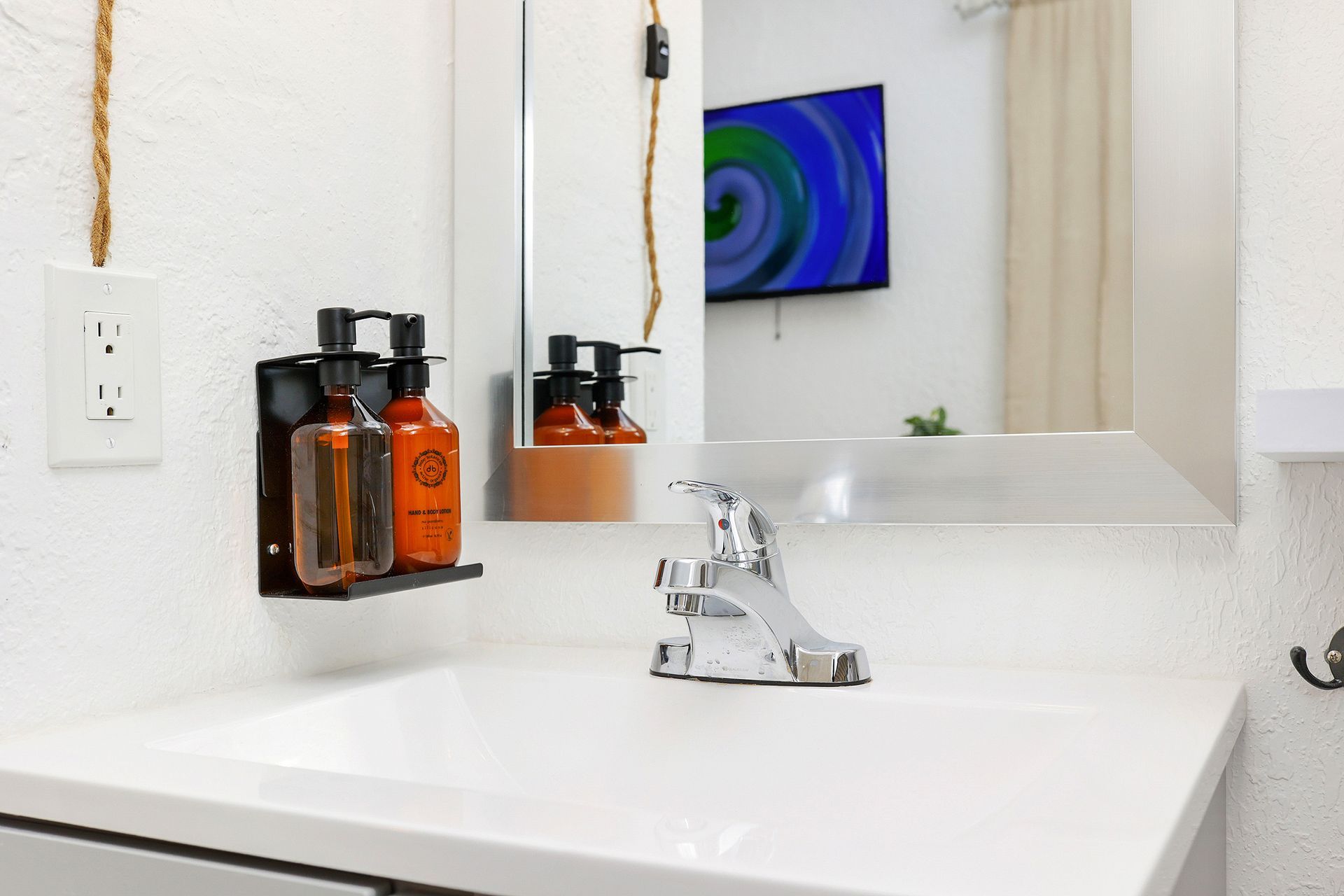 Bathroom sink with a mounted soap dispenser, mirror, and a television in the background.