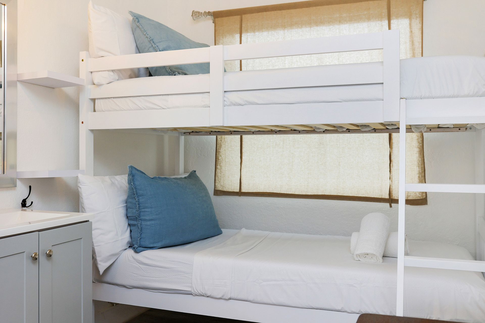 White bunk beds with blue pillows in a bright room with a small window.