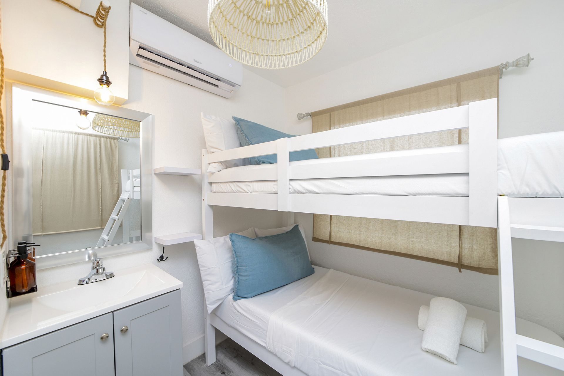 White bunk beds in a room with a sink and a window. Light blue accents.