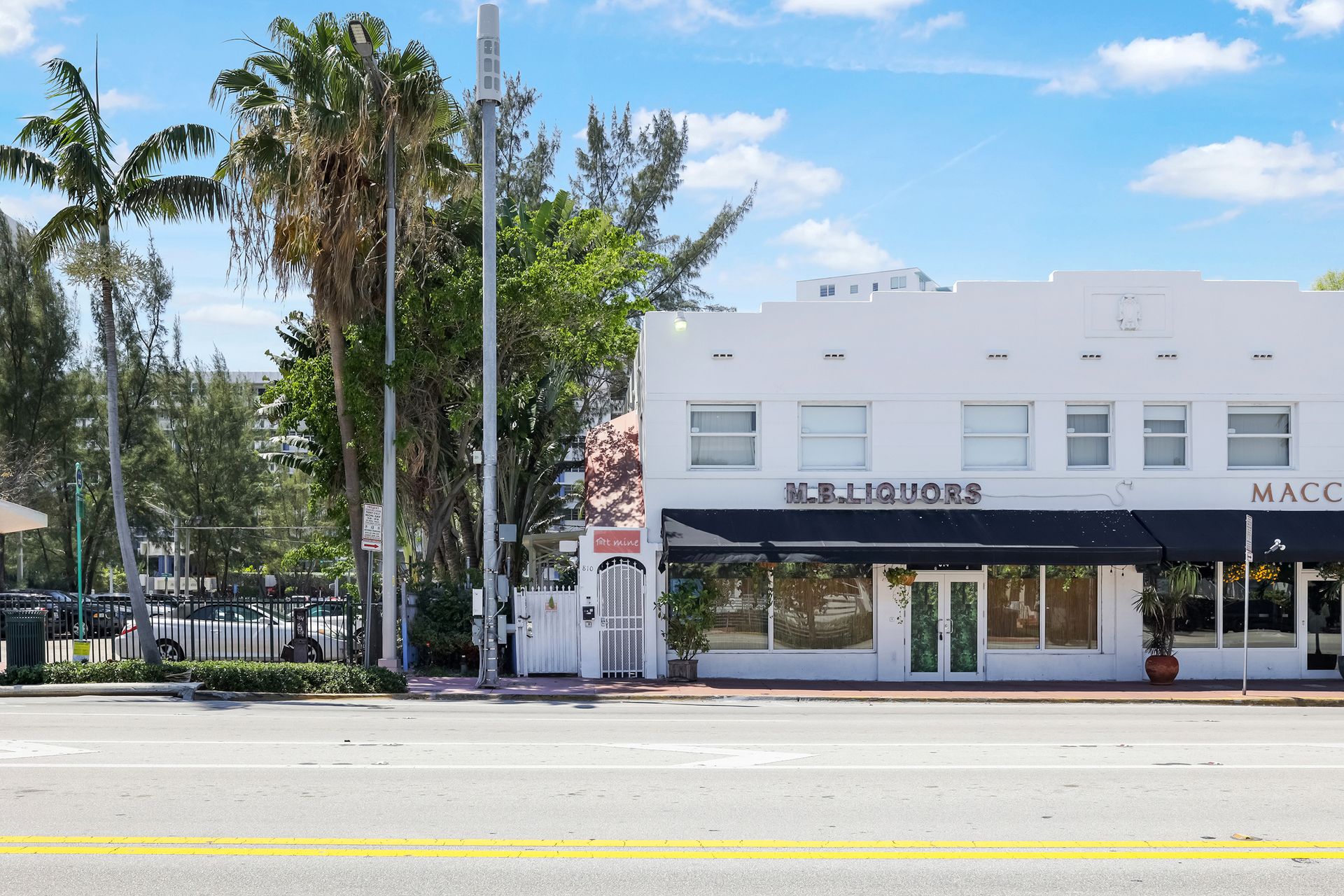 White building with black awning and signage, trees in front.