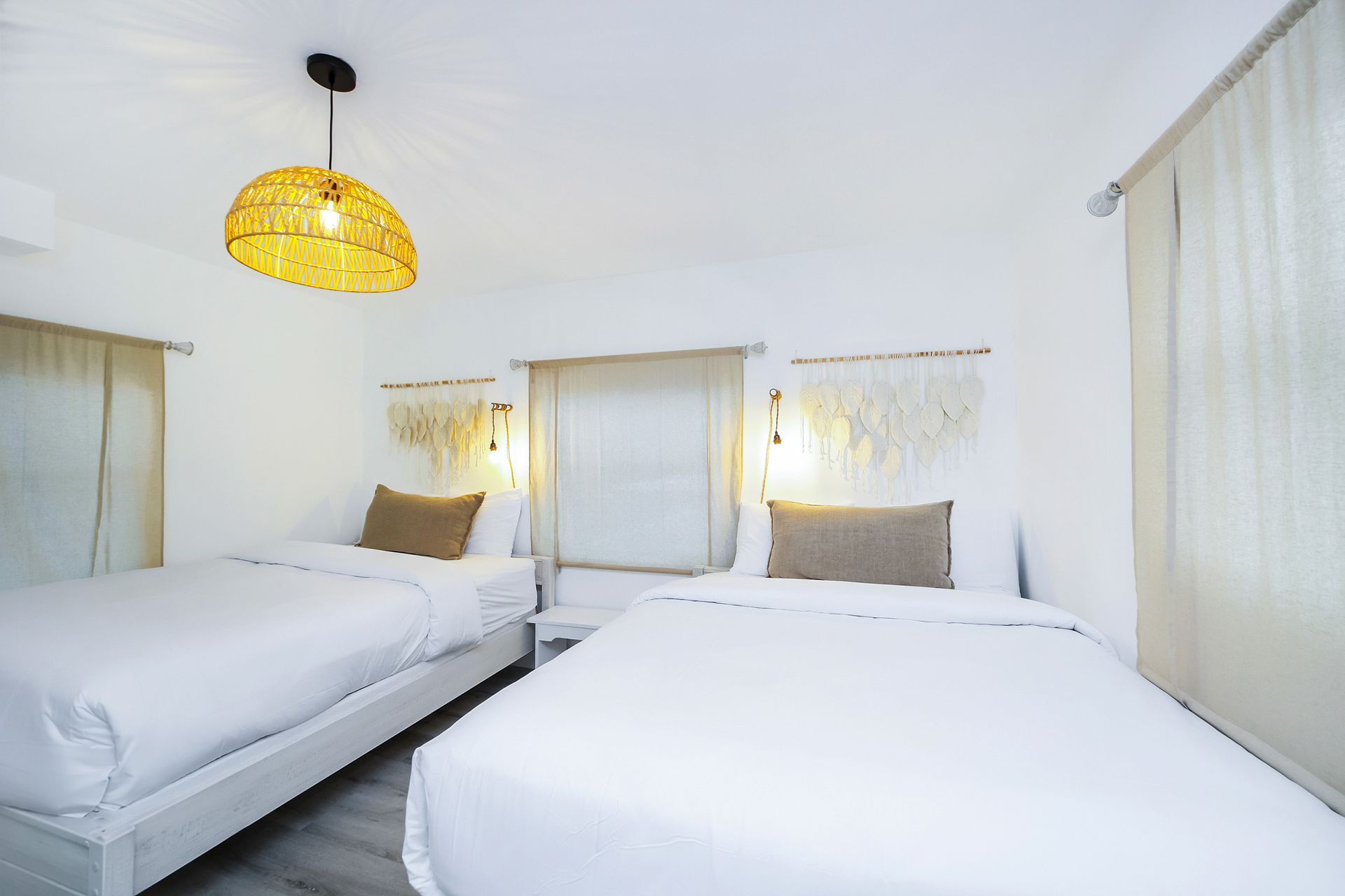 Two beds in a white bedroom with woven light fixtures and textured wall hangings.