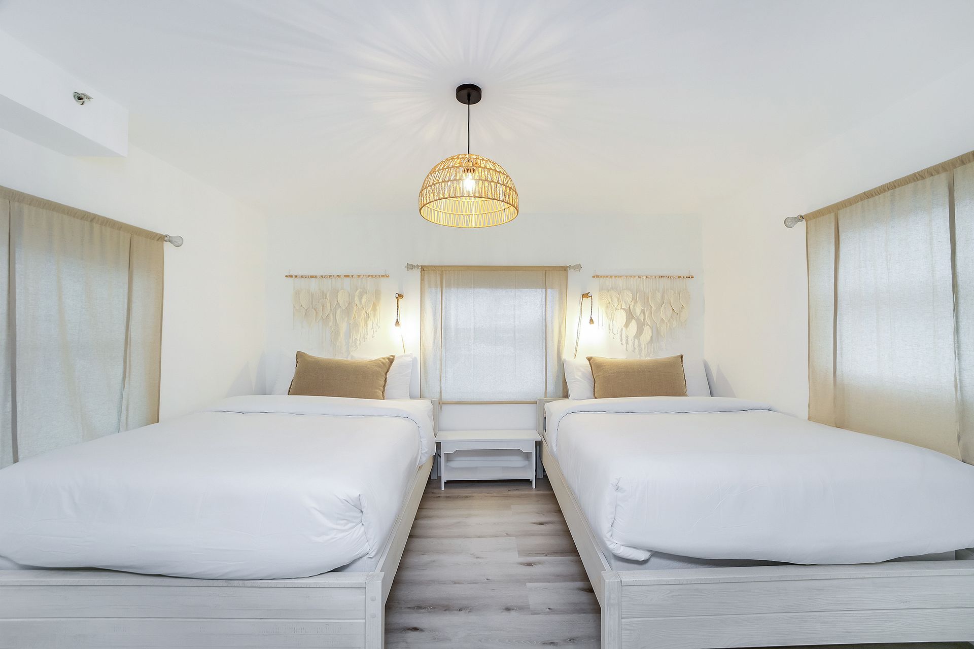 Two twin beds in a bright, white bedroom; decorative light fixture hangs above.