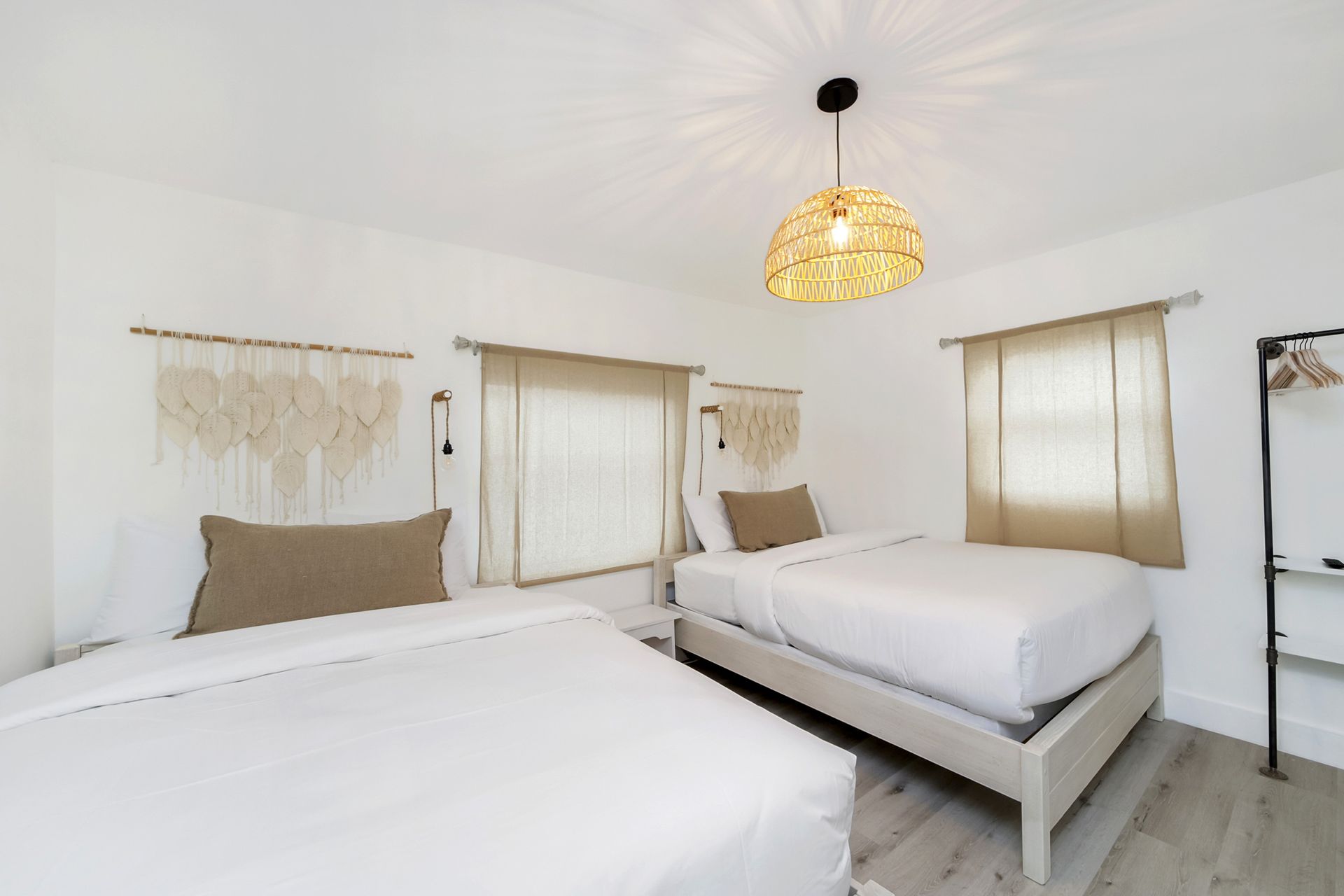 Bedroom with two beds, white walls, woven light fixture, tan curtains, macrame wall hangings.
