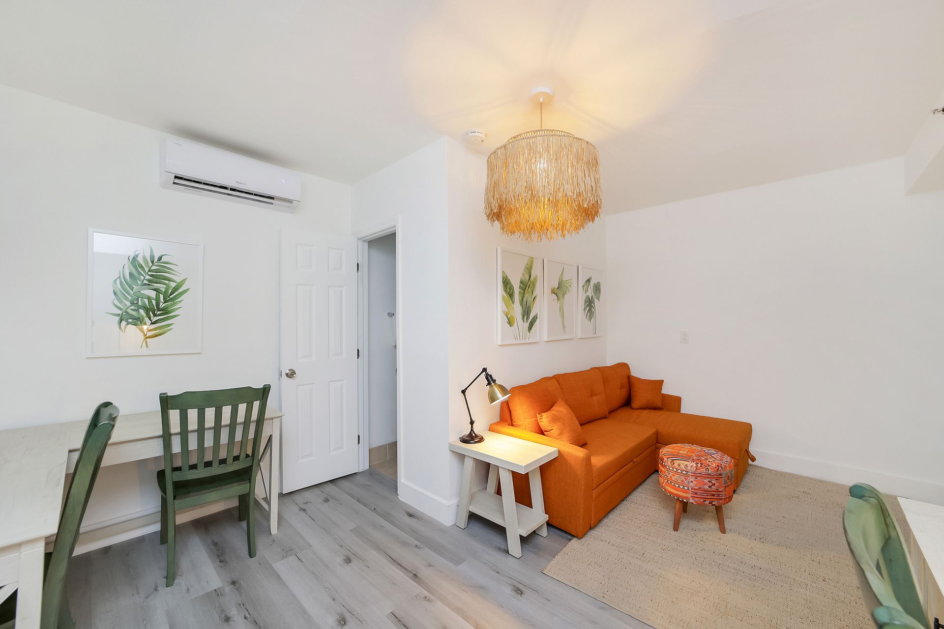 Bright living room with orange couch, desk, and botanical art on white walls.