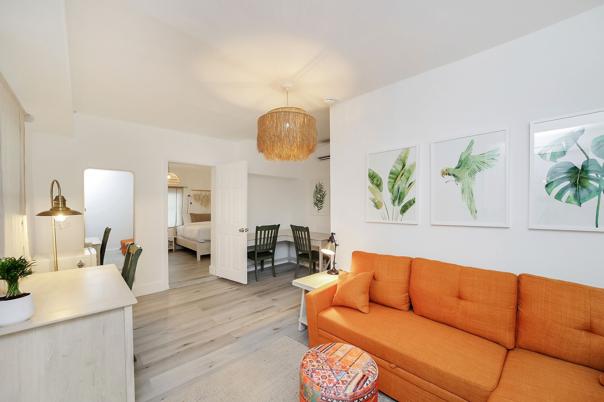 Bright living room with orange sofa, botanical art, and wood floors.